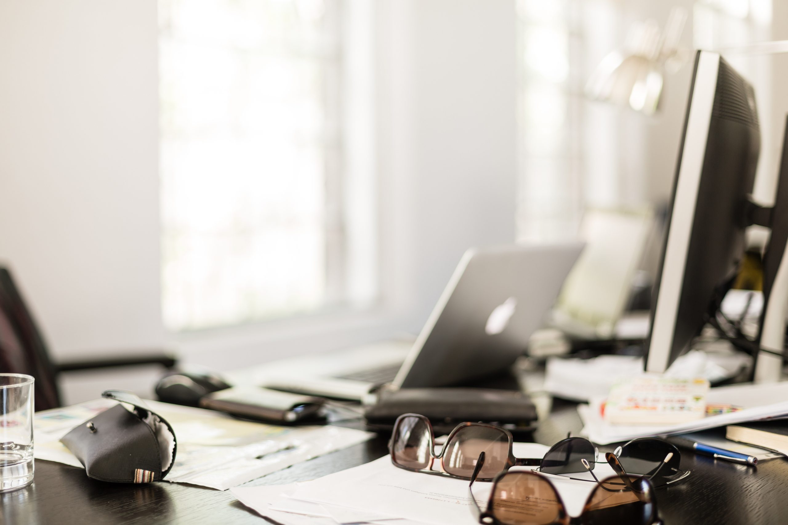 A laptop, a monitor and three pairs of sunglasses on a desk