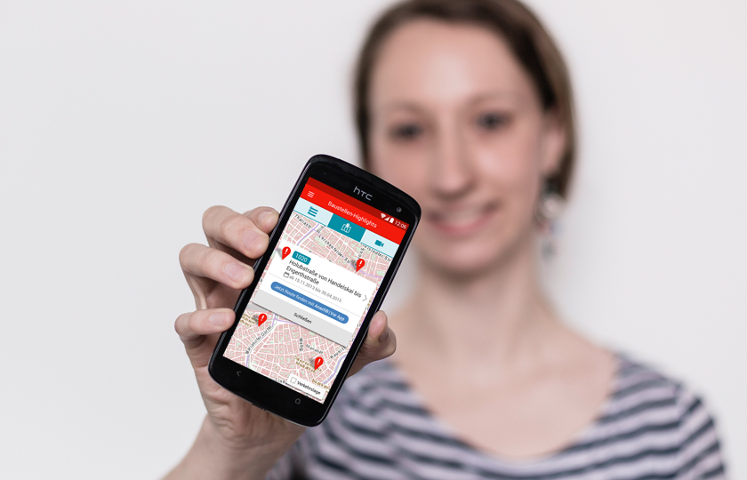 Eine Frau hält ein Handy in die Kamera, darauf die Baustellen App.