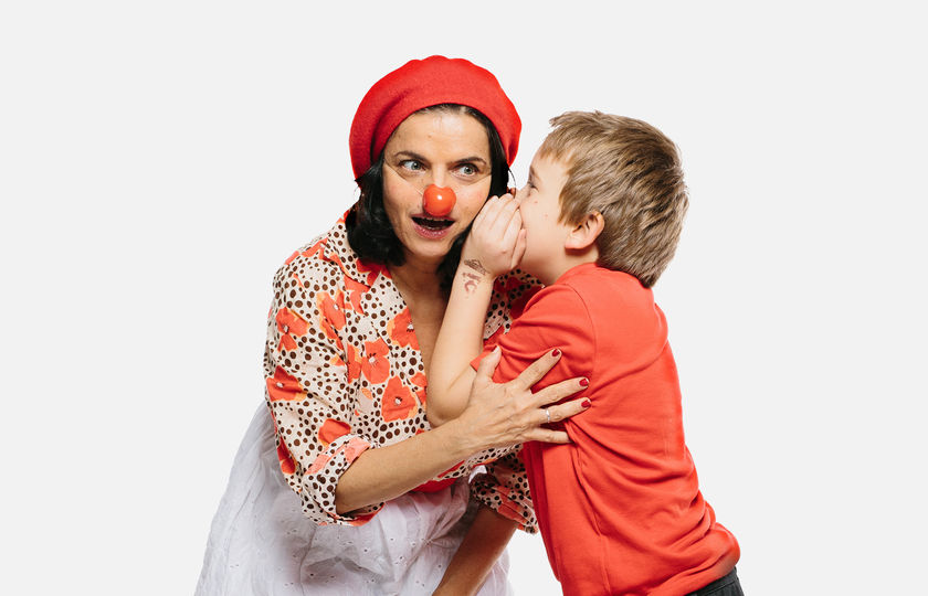 Ein Junge flüstert einer Frau mit Clownsnase etwas ins Ohr.